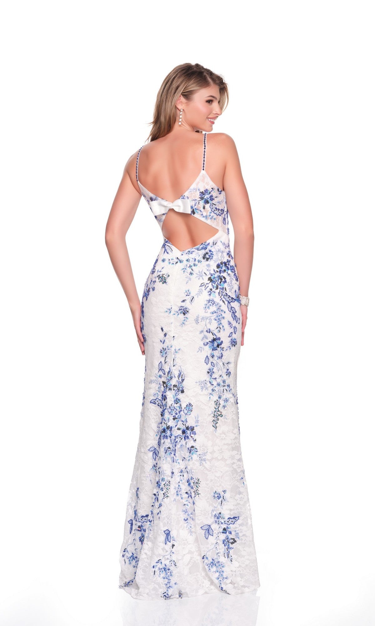 A woman models the Dave and Johnny 12877 long prom dress, a white floor-length gown with blue floral patterns, corset bodice, and open back, as she stands facing away from the camera against a plain white background.